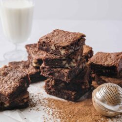 Homemade chocolate brownie bars with nuts and cocoa powder on parchment paper.