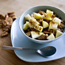 Creamy potato salad with chopped hard-boiled eggs and seasonings in a bowl on a wooden surface.