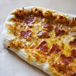 Fresh homemade pepperoni pizza on baking paper, cheesy and delicious.