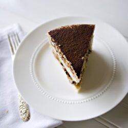 Rich chocolate tiramisu on white plate with powdered cocoa topping, served as a delicious dessert.