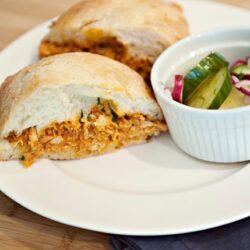 Golden fried chicken sandwich with pickles and onion slaw on a white plate.