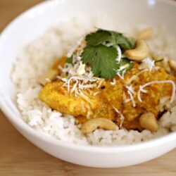 Savory curry chicken served over white rice with cilantro and cashews in a white bowl.