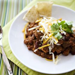 Hearty chili topped with shredded cheese and cilantro on a white plate.