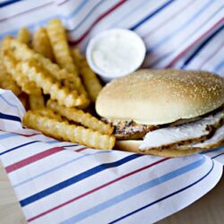 Golden waffle fries with creamy dipping sauce and crispy grilled chicken sandwich on a bun.