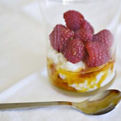 Fresh raspberries on creamy dessert with honey drizzle in a glass, served as a delicious baked treat.