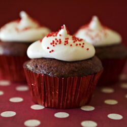 Chocolate cupcakes with vanilla frosting and red sprinkles on a red and white polka dot background.