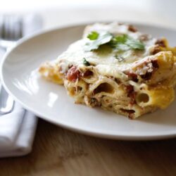 Creamy baked pasta casserole with cheese and herbs served on a white plate.