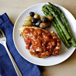 Roasted chicken breast with tomato sauce, asparagus, and new potatoes on white plate.
