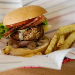 Juicy burger with crispy fries on a lined paper tray.