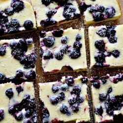 Blueberry cheesecake squares with a creamy filling and fresh blueberries pattern, dusted with powdered sugar.