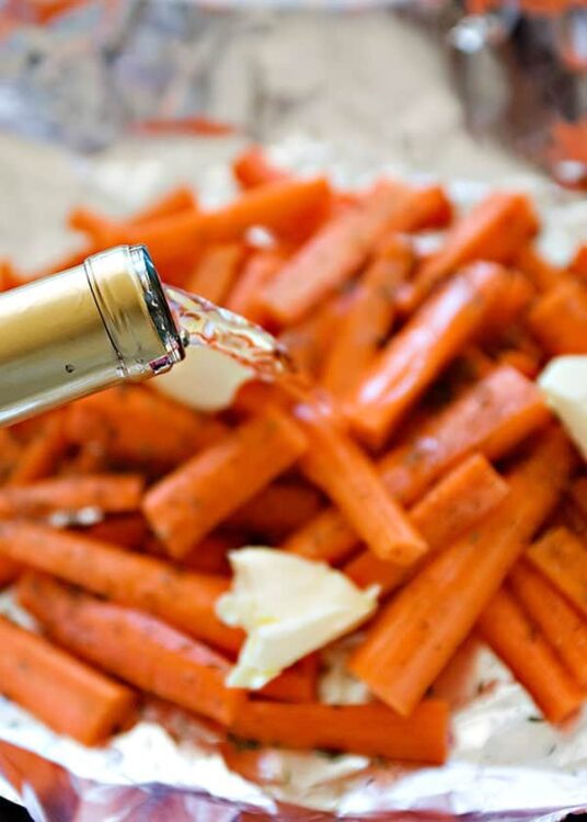 Golden honey being poured over roasted carrots with butter in a baking dish.