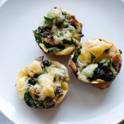 Savory vegetable and cheese muffins with spinach and herbs on white plate.