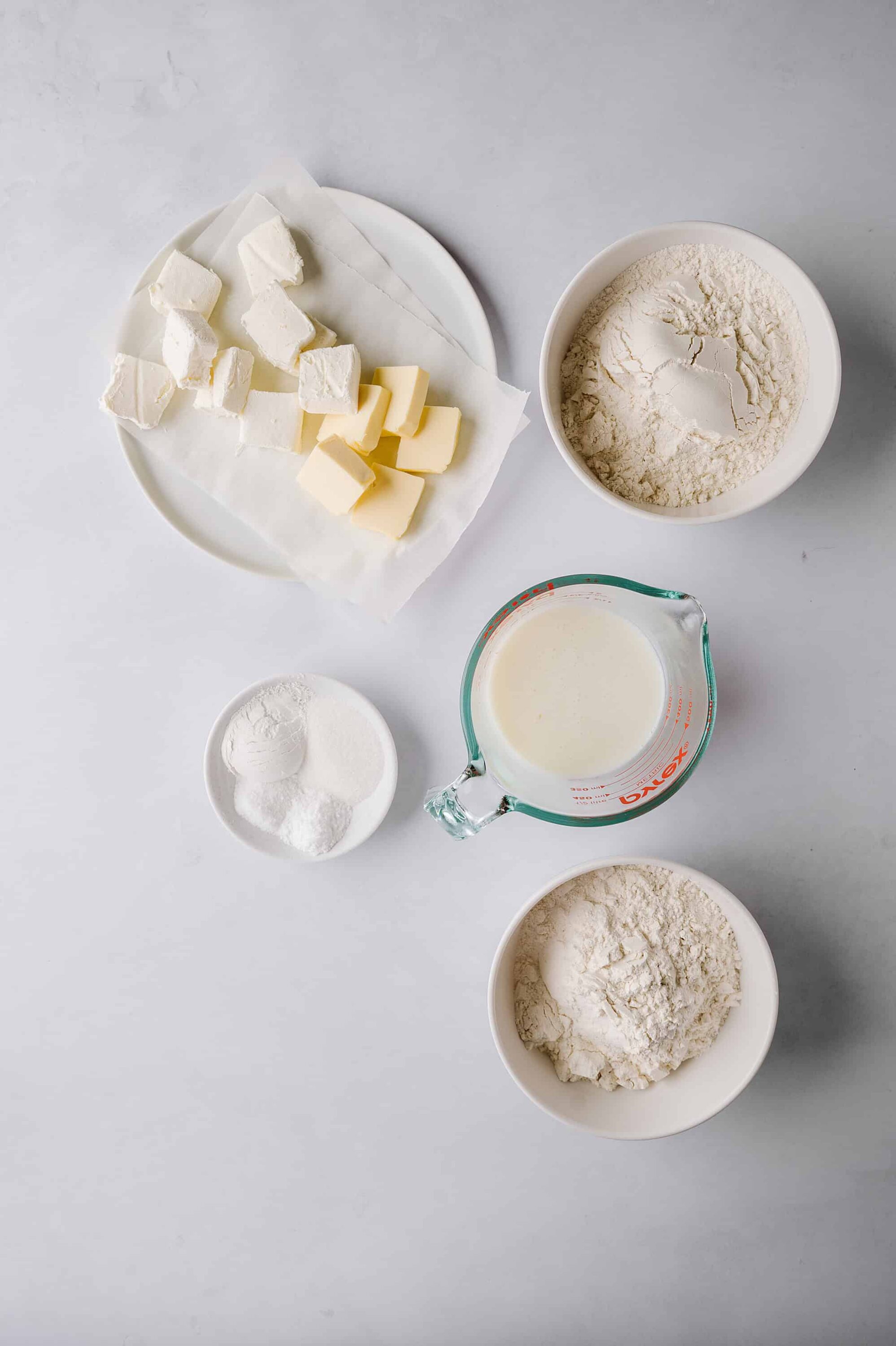 Cream cheese, butter, flour, milk, and sugar arranged on a white countertop for baking.