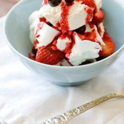Fresh strawberry shortcake with whipped cream and blueberry topping in a light blue bowl.