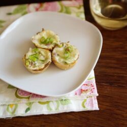 Golden baked stuffed mushroom caps topped with green onions served on a white plate.