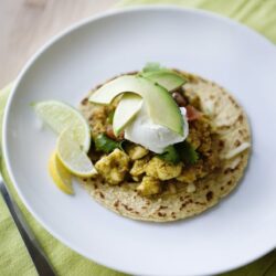 Creamy avocado and poached egg tacos on corn tortilla with lemon wedges.