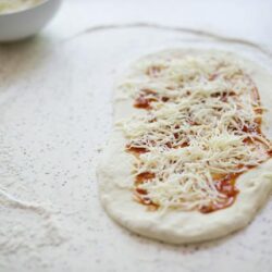 Shaping homemade pizza dough with tomato sauce and shredded cheese.