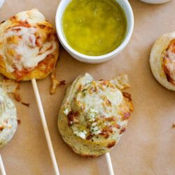 Cheese stuffed garlic bread bites on skewers with dipping sauces and herbs.