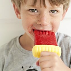 Blueberry popsicle on a child's hand, smiling boy enjoying cooling dessert, healthy summer treat, Baked Bree recipe.
