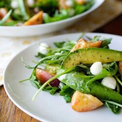 Fresh mixed green salad with avocado, apple slices, and mozzarella cheese on a white plate.