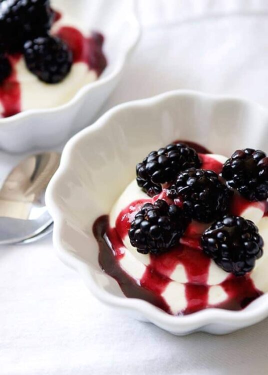 Fresh blackberry and raspberry cheesecake topped with berry sauce in white ramekin, classic dessert recipe.