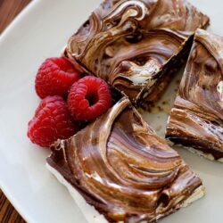 Marble cheesecake bars with raspberries on white plate.