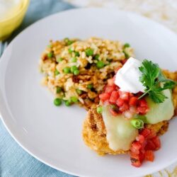 Savory fried fish with melted cheese, fresh salsa, and cilantro served with seasoned rice and peas on a white plate.