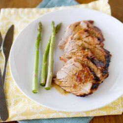 Succulent roast pork tenderloin with asparagus spears on white plate, baked for a perfect dinner.