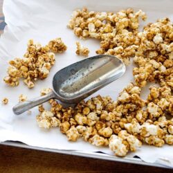 Crispy caramel popcorn on baking sheet with metal scoop.