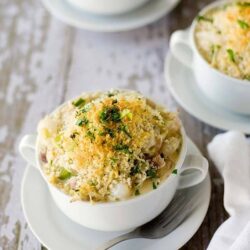 Creamy scalloped potato casserole with cheese and herbs in small white bowls.