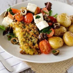 Roasted baby potatoes with fresh tomato and feta salad on a white plate, rustic table setting.