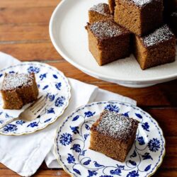Rich, moist brown sugar cake squares dusted with powdered sugar on elegant blue and white plates. Perfect for dessert or teatime.