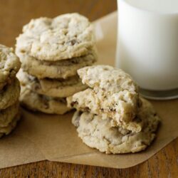 Buttery chocolate chip cookies with a glass of milk on a wooden surface. Perfect for a sweet treat or dessert.