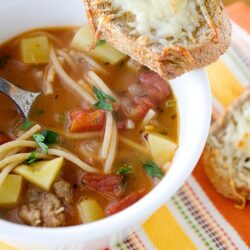 Hearty beef vegetable soup with cheese garlic bread on the side, perfect for cozy meals.