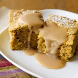 Rich caramel sauce drizzling over moist pumpkin spice cake pieces on a white plate. Perfect fall dessert recipe from Baked Bree.