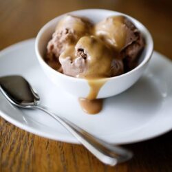 Rich vanilla ice cream with caramel sauce in a white bowl, served on a wooden table.