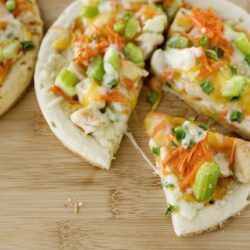 Fresh homemade chicken tacos with cheese, lettuce, and carrots on a wooden surface.