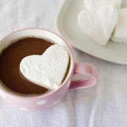 Heart-shaped marshmallow in a pink mug of hot chocolate with marshmallows on a white plate.