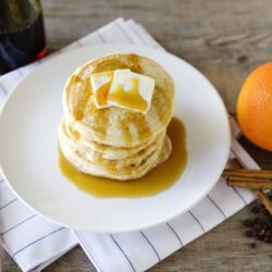 Fluffy stack of buttermilk pancakes topped with butter and syrup on a white plate.