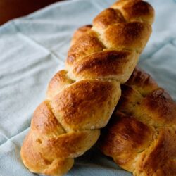 Freshly baked braided bread on a light blue cloth, golden crust, homemade baked goodies.
