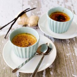 Creamy vanilla crème brûlée served in light blue ramekins on white plates, with rustic wooden background.