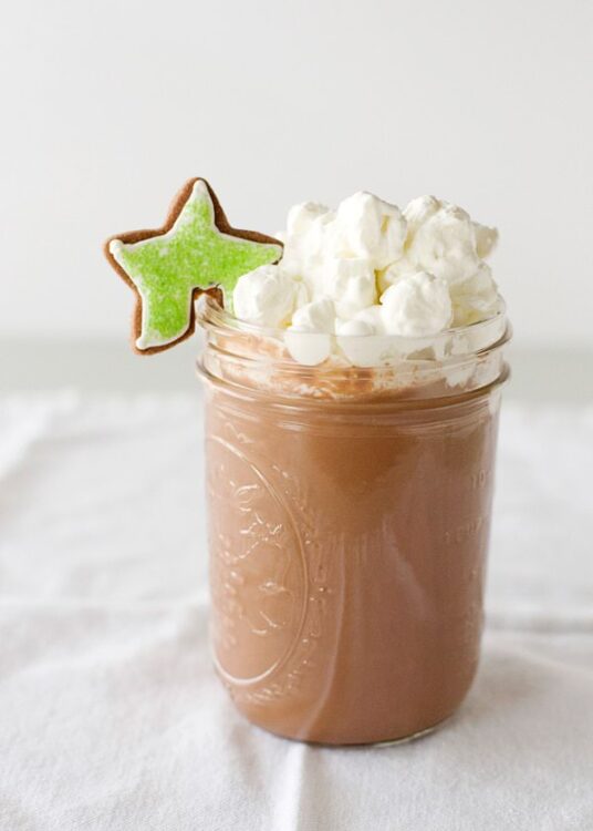 Creamy hot chocolate in a glass jar topped with whipped cream and a festive star-shaped cookie. Perfect winter beverage.