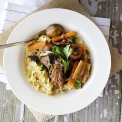 Savory beef and vegetable noodle soup in a white bowl with fresh herbs and roasted potatoes.