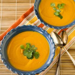 Creamy pumpkin soup garnished with fresh cilantro in blue bowls on a striped napkin, perfect for cozy fall meals.