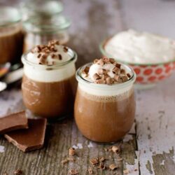 Creamy hot chocolate with whipped cream and chocolate shavings in glass jars.