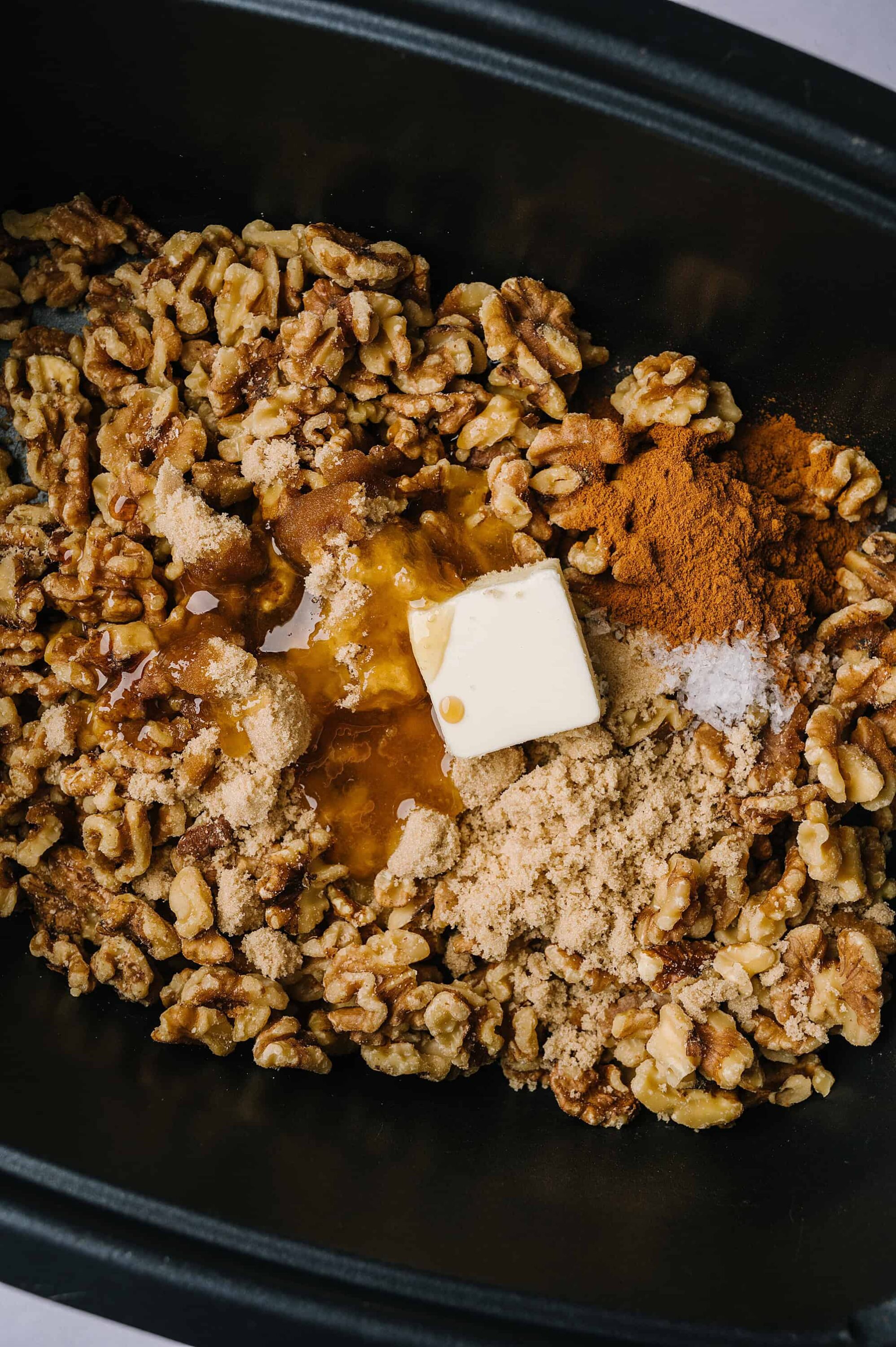 Butter, brown sugar, walnuts, cinnamon, and seasonings in a baking dish for dessert recipe.