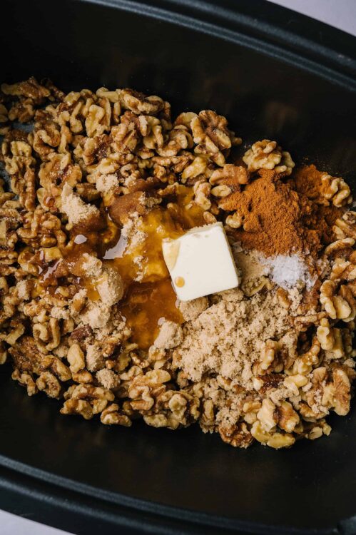 Butter, brown sugar, walnuts, cinnamon, and seasonings in a baking dish for dessert recipe.
