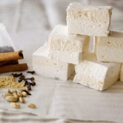 Coconut marshmallows with spices, cinnamon, and vanilla on a rustic wooden background with baking ingredients.