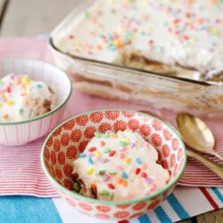 Colorful sprinkle frosted cupcakes in decorative bowls, perfect for dessert or party treats.