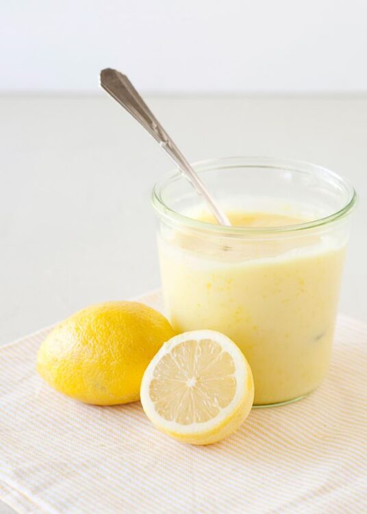 Freshly made lemon curd in a glass bowl with a lemon and half lemon, perfect for baking and dessert recipes.